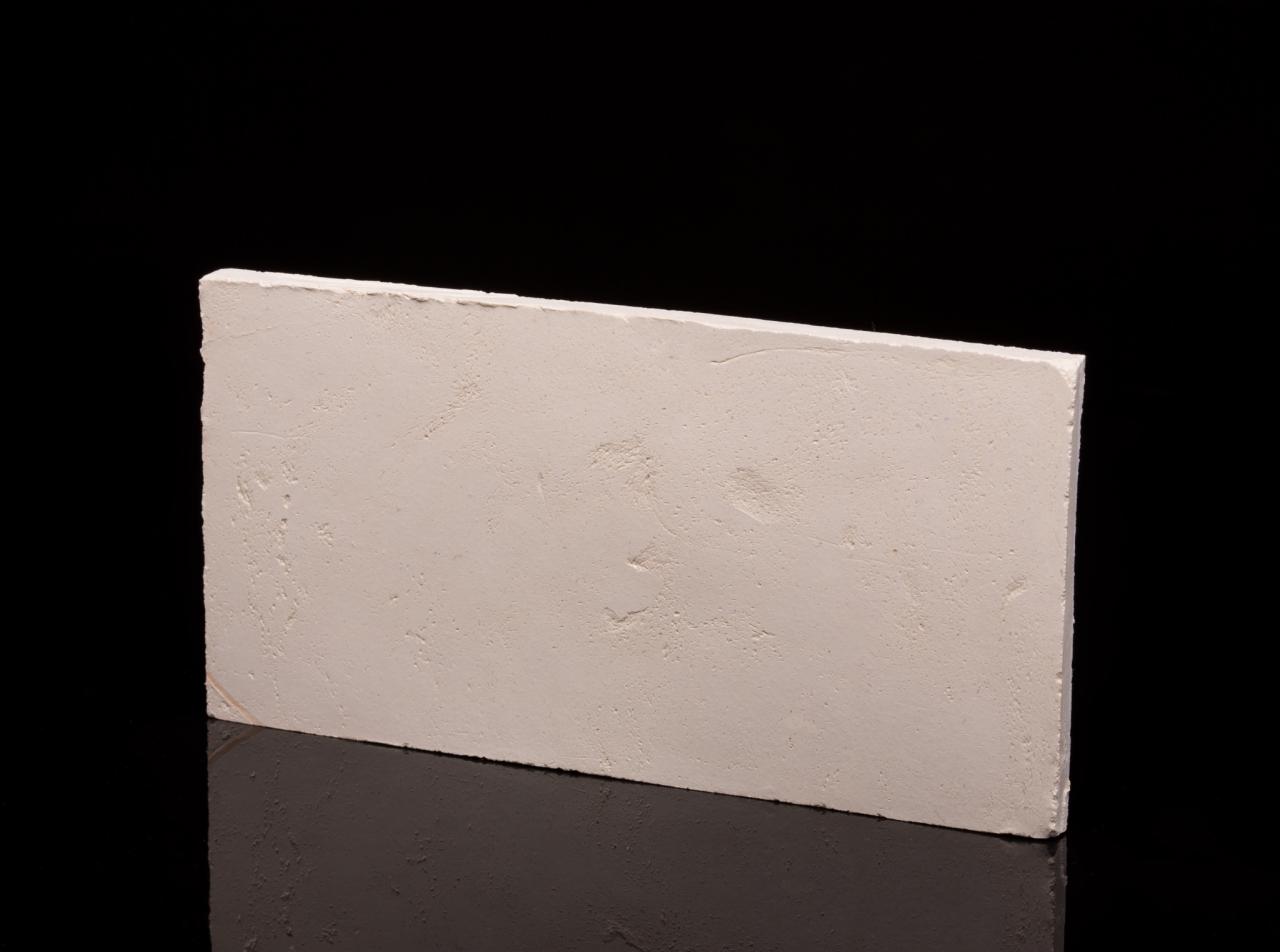 Pojedynczy, prostokątny panel ścienny z jasną, chropowatą fakturą, ustawiony na błyszczącej, ciemnej powierzchni, odbijający światło na czarnym tle.