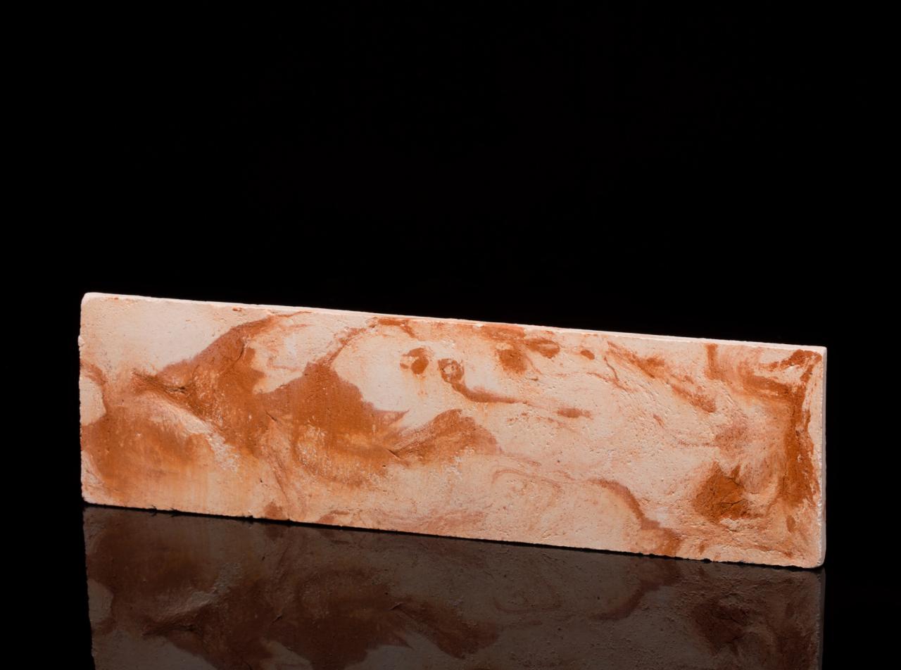 Prostokątna płytka imitująca marmur w odcieniach beżu i brązu, ułożona na czarnej, błyszczącej powierzchni, odbijająca światło.