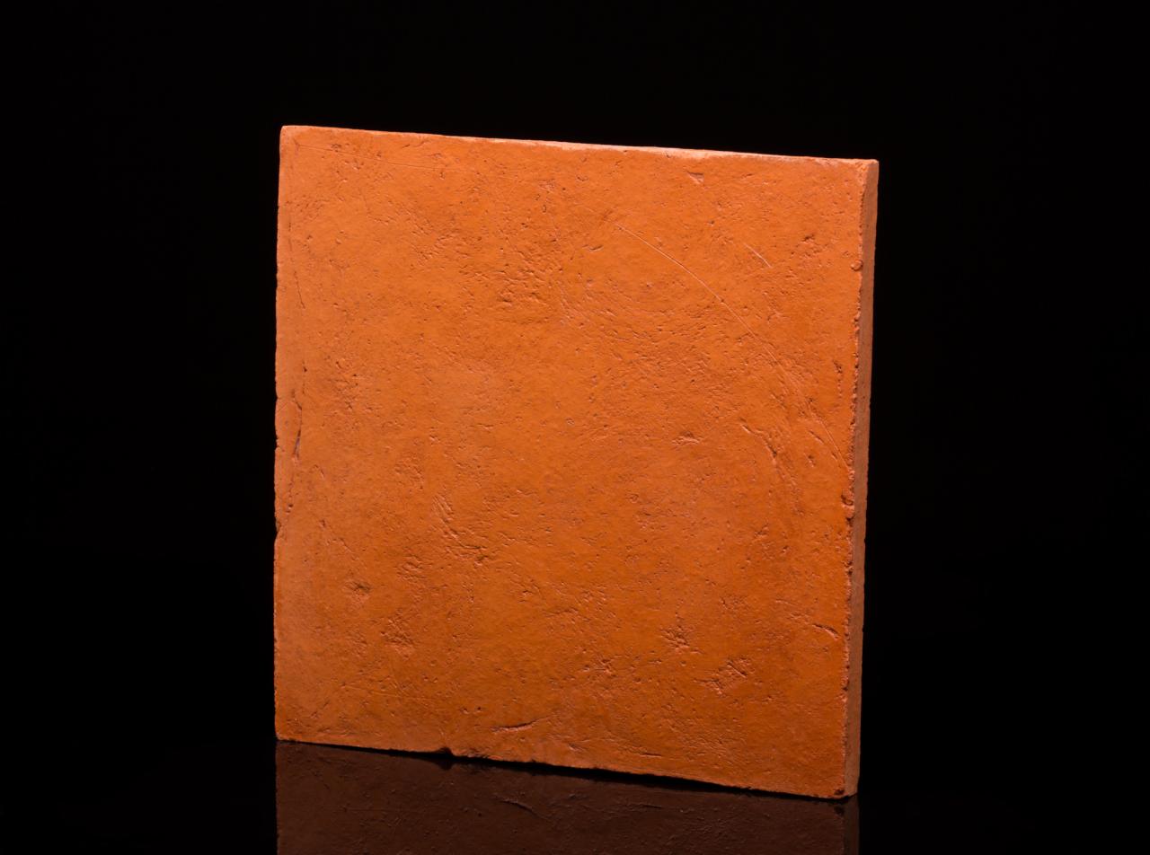 Pomarańczowa próbka panela o wyraźnej fakturze na czarnym, refleksyjnym tle.