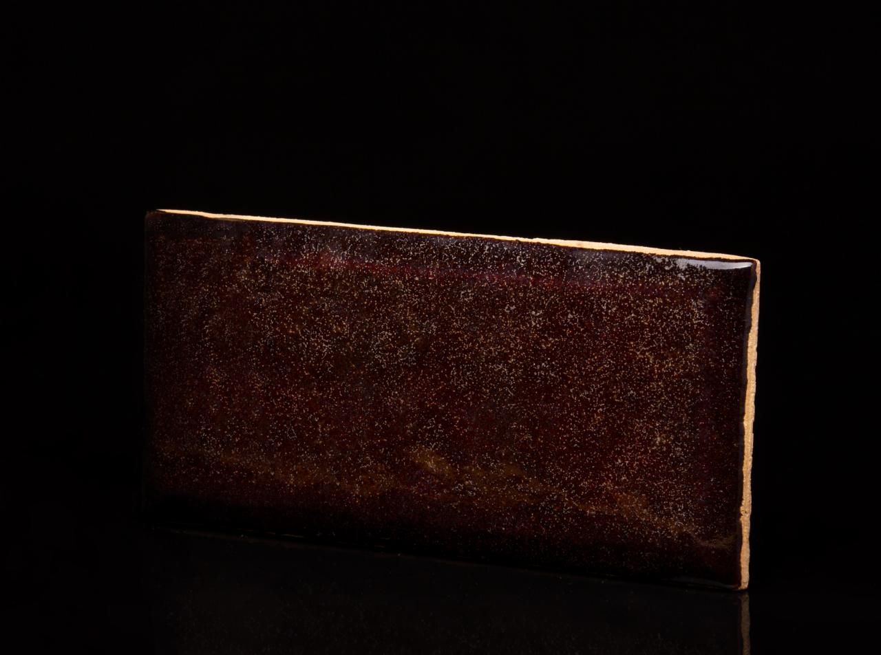 Pojedynczy, prostokątny panel w odcieniach brązu z delikatną, połyskującą fakturą na czarnym tle, widoczny z bliska.