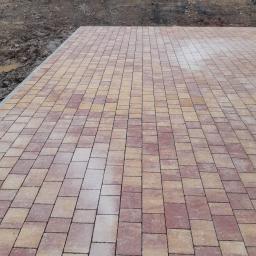 PROBUD Krzysztof Gołda - Ułożona kostka brukowa w odcieniach czerwieni i beżu, widok z góry na nową nawierzchnię, z ziemią w tle.