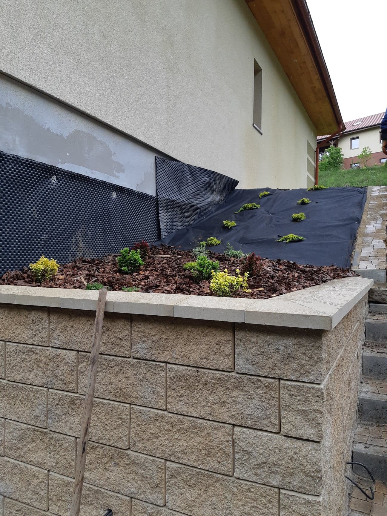 Budowa muru oporowego z kostki w Jedlinie-Zdroju, widoczna izolacja pionowa fundamentów oraz przygotowanie terenu pod nasadzenia.