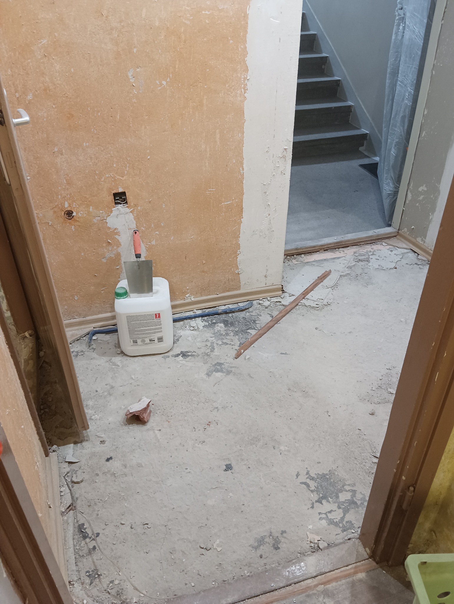 Przygotowanie do remontu w Żorach: wiadro z klejem, kielnia i fragment cegły na zakurzonym podłożu, ściany częściowo przygotowane do malowania, widoczne schody.