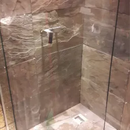 Wykończona kabina prysznicowa z brązowymi płytkami imitującymi kamień, z odpływem liniowym w rogu, widoczne ślady po fugowaniu i czyszczeniu.