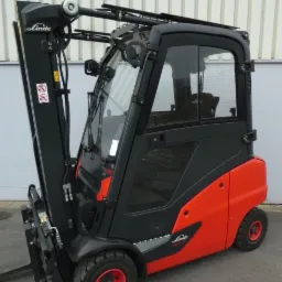 Nowy wózek widłowy Linde H20D, pomarańczowo-czarny, z kabiną, na tle szarej ściany z blachy falistej.