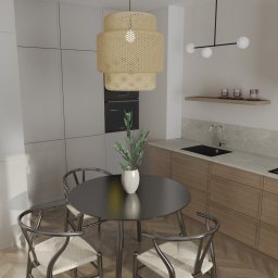 ARANŻ Joanna Gościańska - Wizualizacja nowoczesnej kuchni z okrągłym, czarnym stołem otoczonym trzema krzesłami z metalową ramą i plecionymi siedziskami, pod ażurową lampą w odcieniach beżu. W tle zabudowa kuchenna...