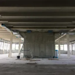 Wnętrze budynku komercyjnego w trakcie instalacji systemu kanałów wentylacyjnych pod sufitem, widoczna drabina oparta o ścianę, surowy stan wykończenia.