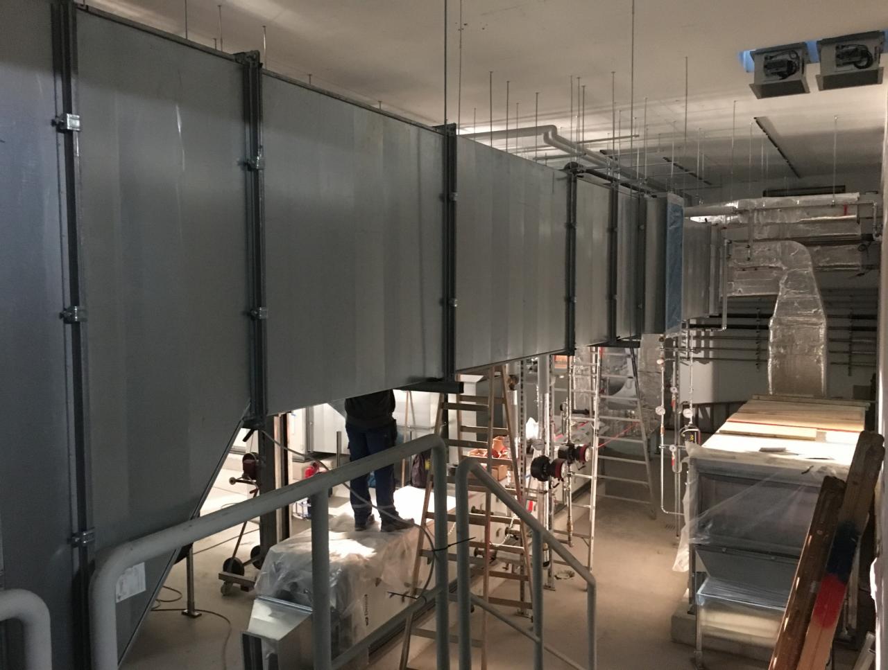 Instalacja systemu kanałów wentylacyjnych w surowym wnętrzu, widoczne drabiny i elementy montażowe.