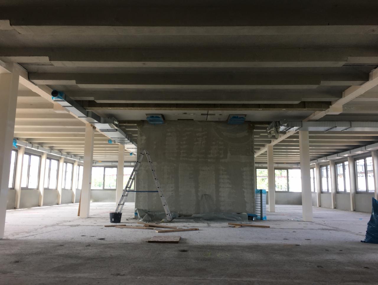 Wnętrze budynku komercyjnego w trakcie instalacji systemu kanałów wentylacyjnych pod sufitem, widoczna drabina oparta o ścianę, surowy stan wykończenia.