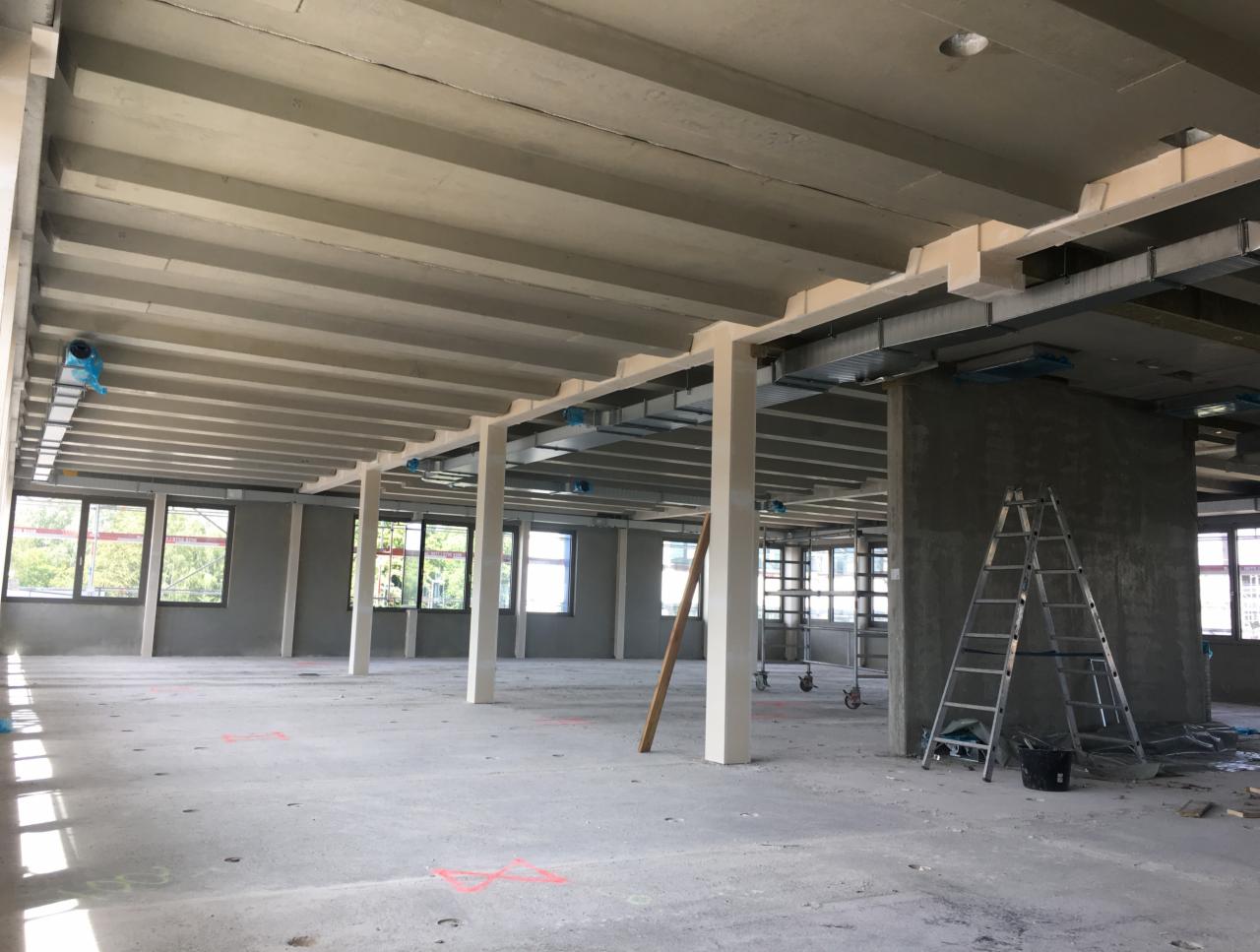 Wnętrze budynku komercyjnego w trakcie montażu instalacji wentylacyjnej, widoczne kanały wentylacyjne pod sufitem, rusztowania i drabina. Część kanałów zabezpieczona folią.