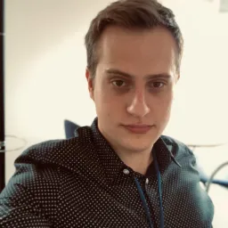 Portret mężczyzny w koszuli w kropki z niebieską smyczą, z bliska, w jasnym pomieszczeniu biurowym. Ujęcie z góry, naturalne oświetlenie.