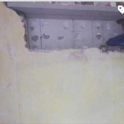 Nasz dom - Fragment ściany z otworem ukazującym szare bloczki izolacyjne, widoczny fragment cegły i dłoń w rękawicy podczas prac wykończeniowych.