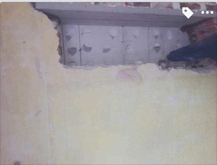 Fragment ściany z otworem ukazującym szare bloczki izolacyjne, widoczny fragment cegły i dłoń w rękawicy podczas prac wykończeniowych.