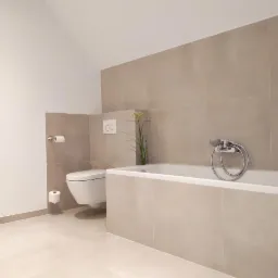 Minimalistyczna łazienka z beżowymi płytkami, wiszącą toaletą i wanną obudowaną płytkami, uzupełniona delikatną dekoracją roślinną.