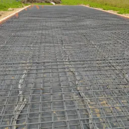 Zbrojenie fundamentu na czarnej folii, widoczne rury wentylacyjne i kopiec ziemi w tle.