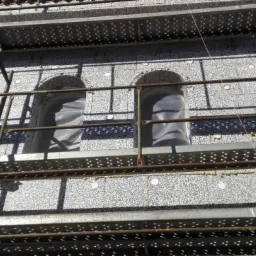 Budynek w trakcie ocieplania elewacji styropianem, widoczne rusztowania i zabezpieczone okna folią.