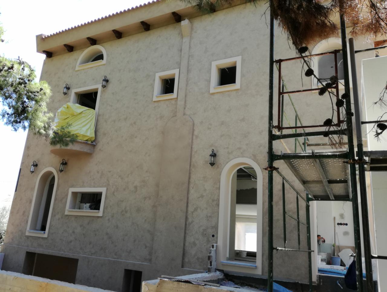 Dwupiętrowy dom z elewacją w odcieniach beżu, widoczne rusztowania i okno zabezpieczone folią, sugerujące prace wykończeniowe.