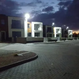 Nowoczesne domy szeregowe oświetlone latarniami ulicznymi, widoczne o zmierzchu z ciemnym niebem w tle.