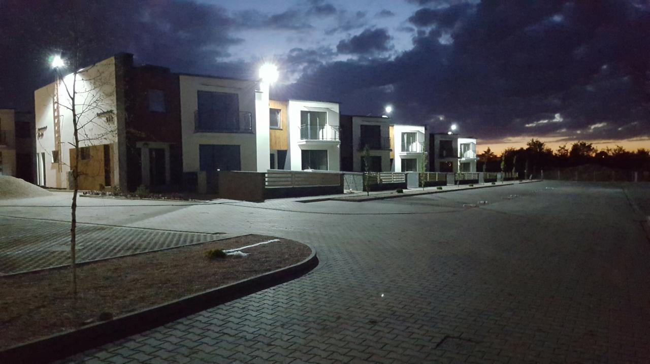 Nowoczesne domy szeregowe oświetlone latarniami ulicznymi, widoczne o zmierzchu z ciemnym niebem w tle.