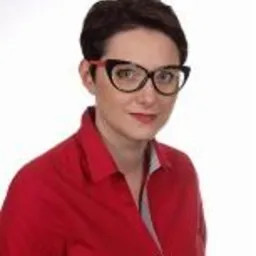 Portret kobiety w czerwonej koszuli i okularach w czarno-czerwonych oprawkach, na jasnym tle. Krótkie, ciemne włosy. Uśmiech. Profesjonalny wizerunek.