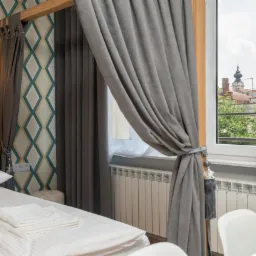 Eleganckie, szare zasłony z dekoracyjnymi wiązaniami w pokoju hotelowym z widokiem na miasto przez okno.