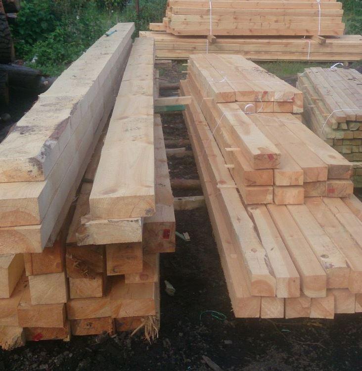 Stosy świeżo przetartego drewna budowlanego, niektóre z korą, ułożone na ziemi i przygotowane do transportu lub dalszej obróbki.