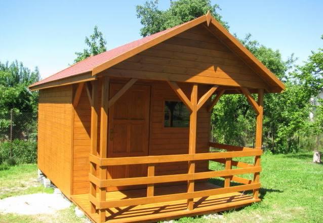 Gotowa, drewniana altana z zadaszeniem i balustradą, pomalowana na brązowo, z czerwoną dachówką, umieszczona na trawniku.