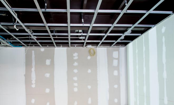 Montaż metalowej konstrukcji sufitu podwieszanego w pomieszczeniu z częściowo wykończonymi ścianami, widoczne przewody elektryczne.