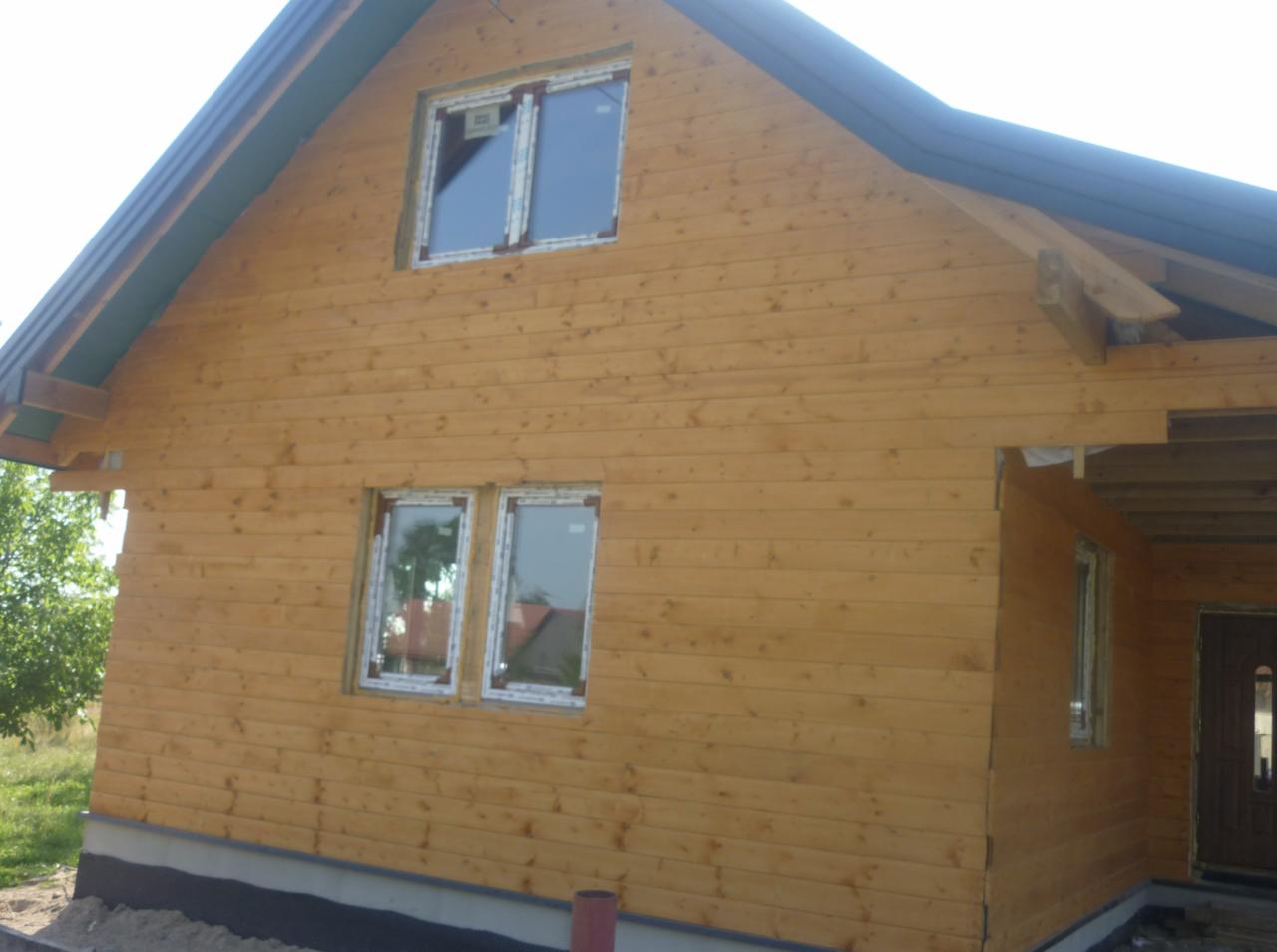 Dom w Folwarkach Wielkich w trakcie budowy, z widoczną drewnianą elewacją, wstawionymi oknami PCV i elementami konstrukcji dachu.