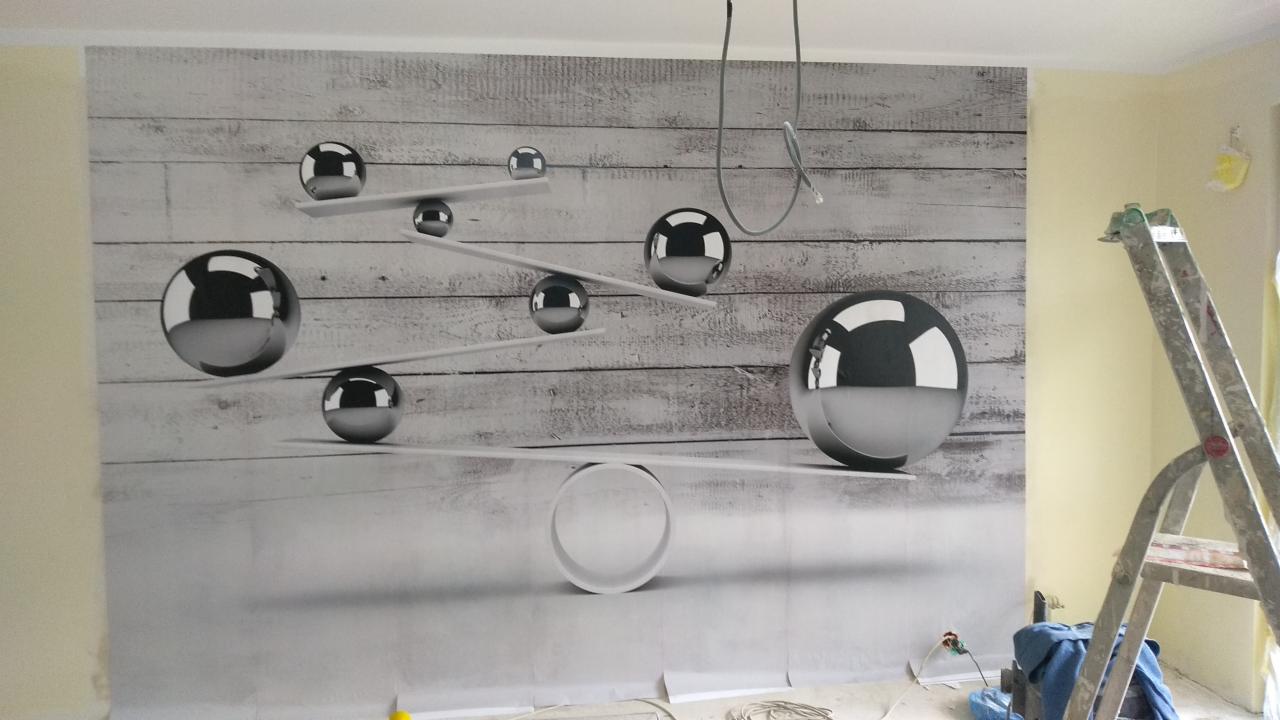 Ściana z fototapetą przedstawiającą srebrne kule na tle imitacji drewnianych desek, widoczna drabina malarska i zabezpieczona podłoga.