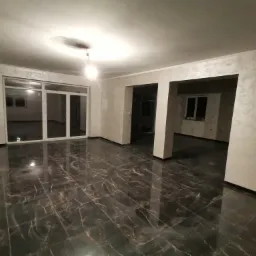 Wnętrze po remoncie: błyszcząca, ciemna marmurowa podłoga, ściany wykończone dekoracyjną strukturą, duże okno balkonowe.