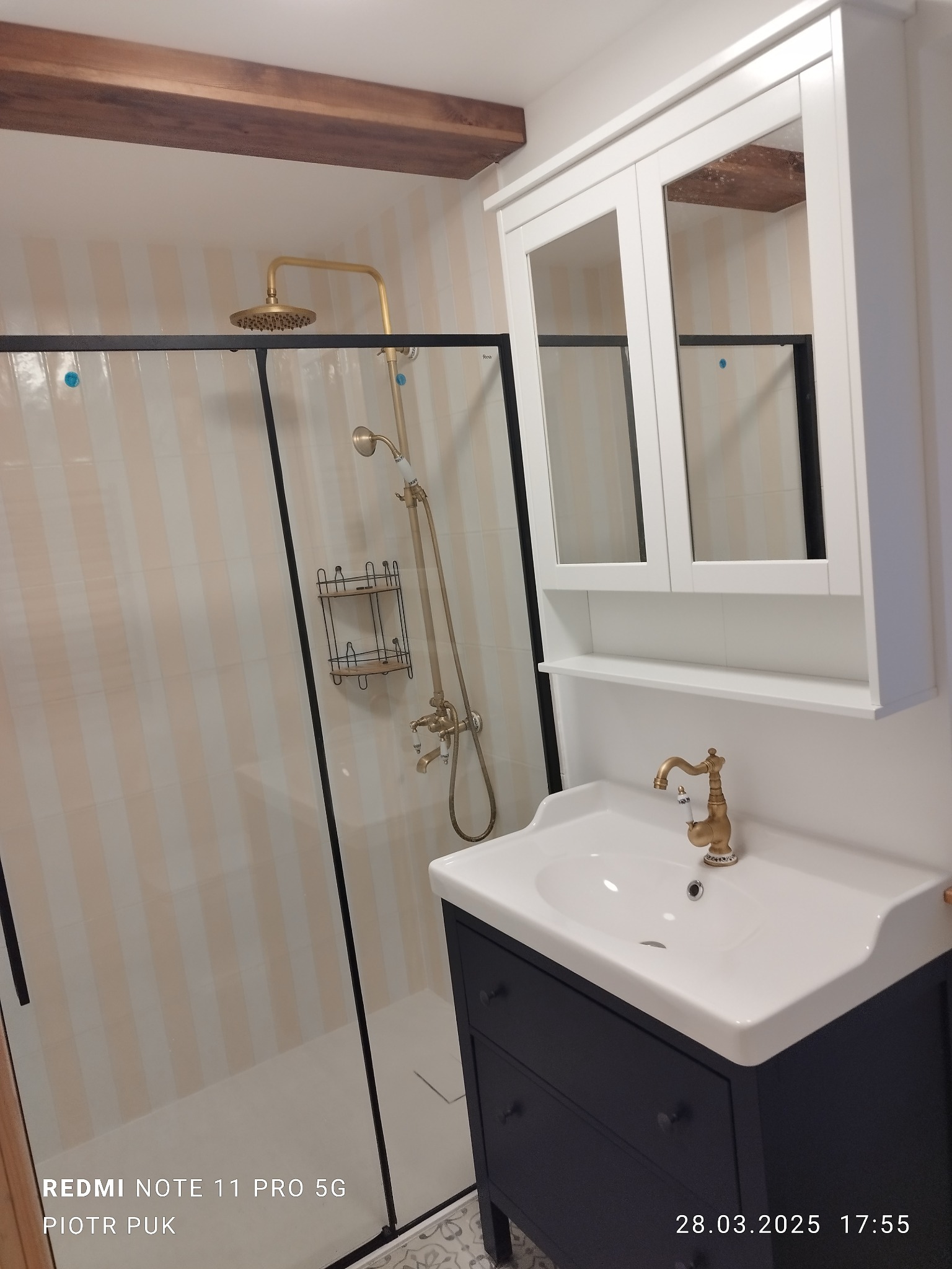 Wykończona łazienka z kabiną prysznicową typu walk-in, złotą armaturą i umywalką z szafką w stylu retro, drewniana belka stropowa.