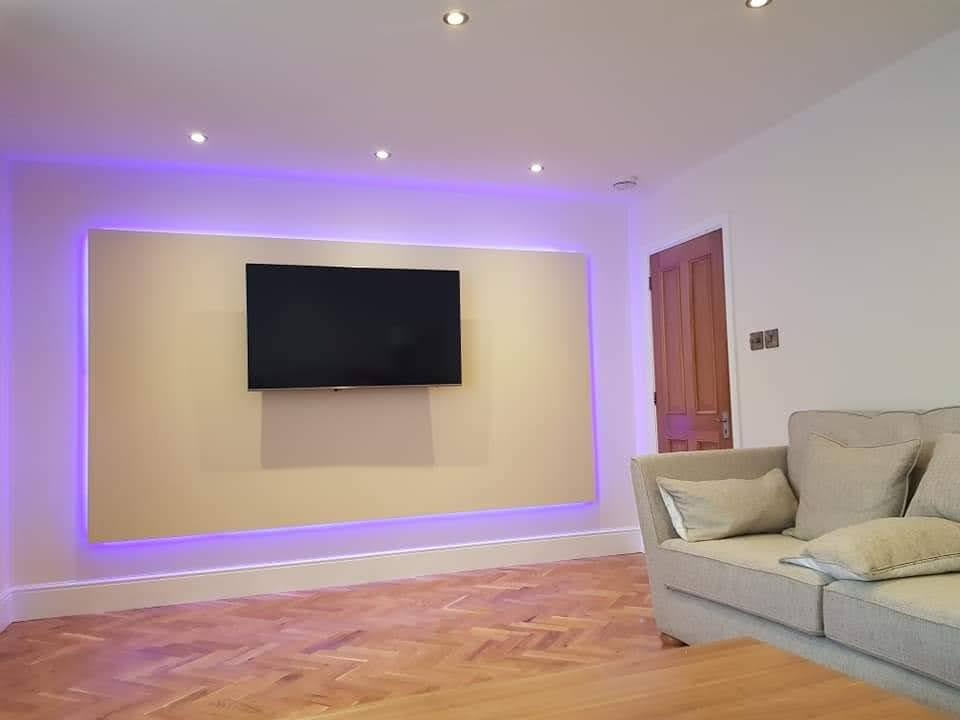 Salon po remoncie: ściana z podświetleniem LED za telewizorem, parkiet w jodełkę, beżowa sofa. Nowoczesne oświetlenie punktowe.