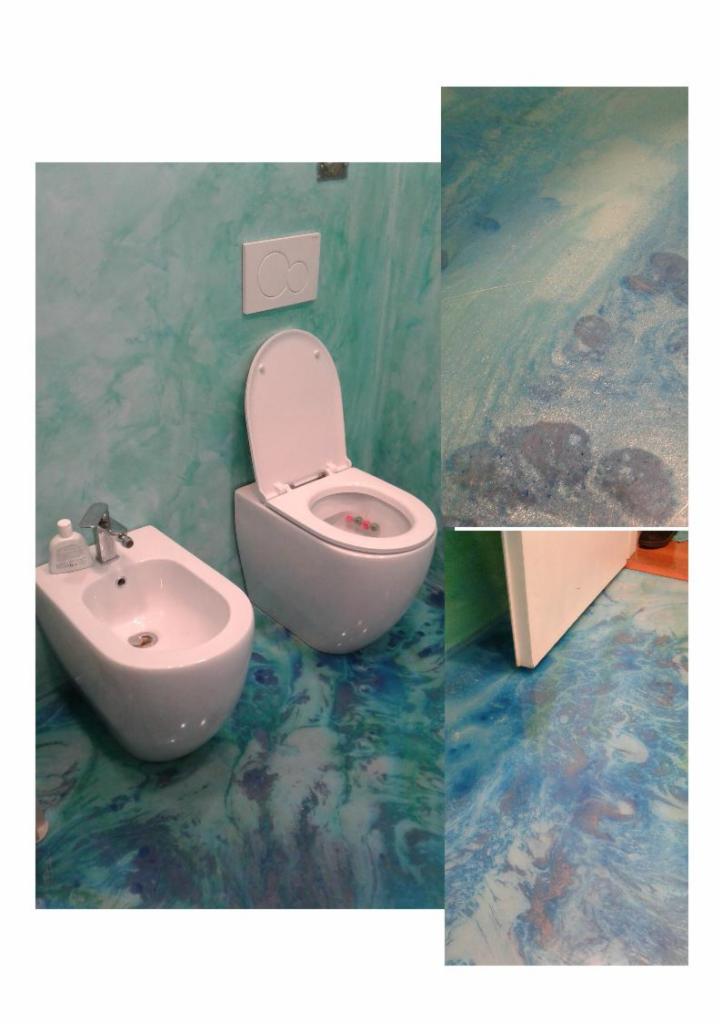 Wykończona łazienka z białą armaturą (WC i bidet) oraz ścianami i podłogą w odcieniach błękitu i zieleni z efektem żywicy, widoczne detale wykończenia podłogi przy drzwiach.