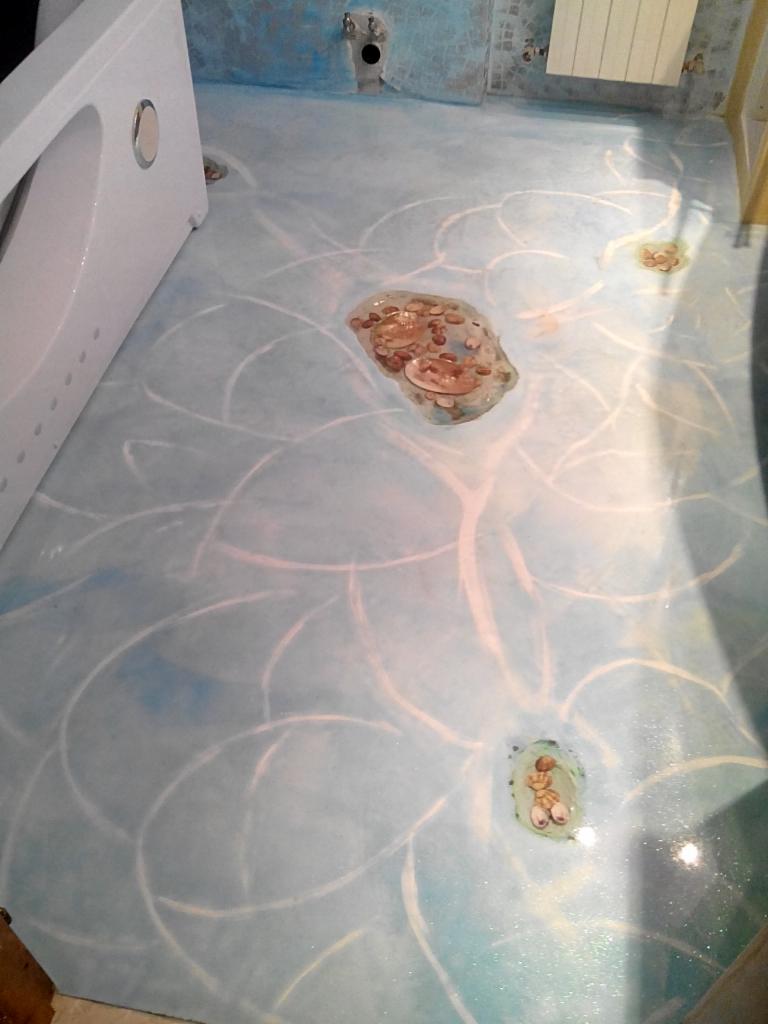 Jasnoniebieska podłoga w łazience z wzorem przypominającym kwiaty i zatopionymi dekoracjami, widoczna wanna po lewej stronie i grzejnik na ścianie w tle.