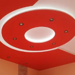 Czerwony sufit podwieszany z okrągłym wgłębieniem oświetlonym białym światłem i punktowymi lampami, kontrastujący z białym fragmentem sufitu.