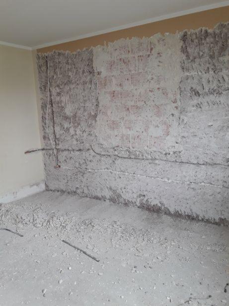 Przygotowanie ściany pod dalsze prace wykończeniowe: usunięte stare warstwy, widoczne fragmenty instalacji elektrycznej, gruz na podłodze.