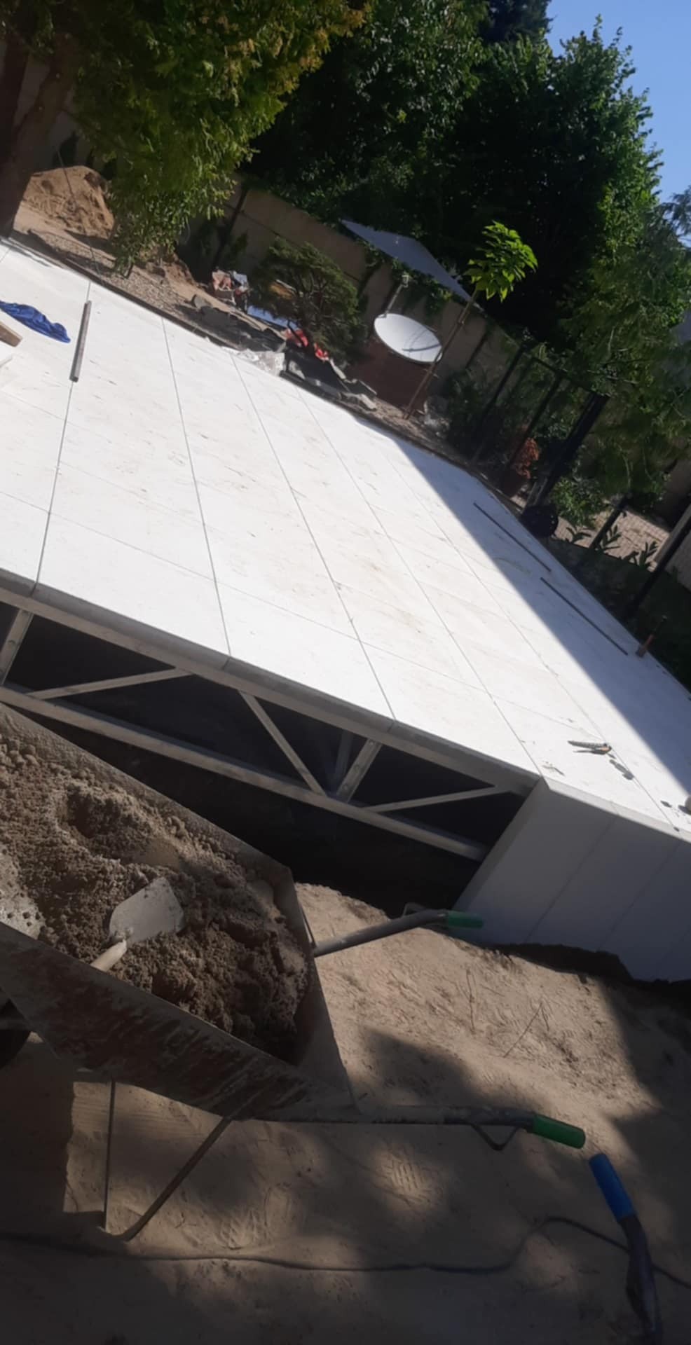 Biała, kwadratowa podłoga z płytek na zewnątrz, z widoczną konstrukcją wsporczą i piaskiem, sugerująca etap budowy lub remontu tarasu.