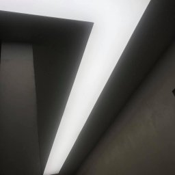 Firma Usługowa Majer - Geometryczna, podświetlana konstrukcja sufitowa w kształcie litery L, z ciemnymi ścianami w tle i delikatną teksturą, oświetlona równomiernym światłem.
