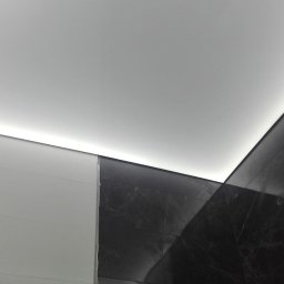 Firma Usługowa Majer - Fragment łazienki z białymi i czarnymi marmurkowymi płytkami, podświetlony sufit LED, widoczne niedociągnięcia w wykończeniu przy łączeniu płytek.