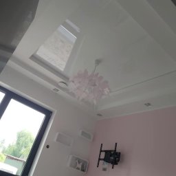 Firma Usługowa Majer - Błyszczący, biały sufit napinany z oknem dachowym i dekoracyjną, różową lampą w pokoju z różową ścianą i zamontowanym uchwytem na telewizor.