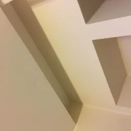 Fragment pomalowanego sufitu z dekoracyjnymi, wystającymi elementami w kolorze złamanej bieli, widoczne pod kątem.