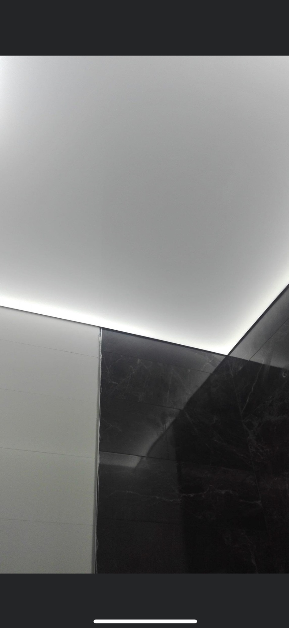 Fragment łazienki z białymi i czarnymi marmurkowymi płytkami, podświetlony sufit LED, widoczne niedociągnięcia w wykończeniu przy łączeniu płytek.