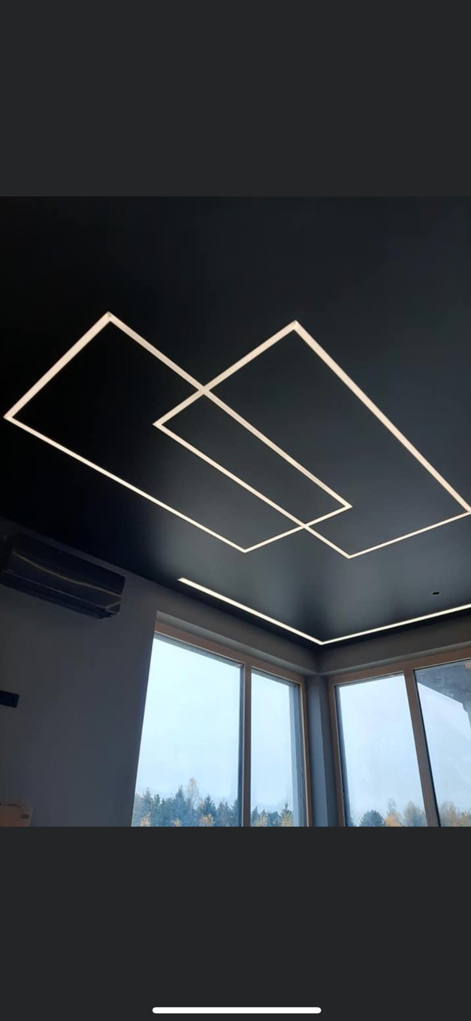 Czarny sufit z geometrycznym oświetleniem LED w kształcie kwadratów, widok na okno z drzewami w tle, klimatyzator na ścianie.