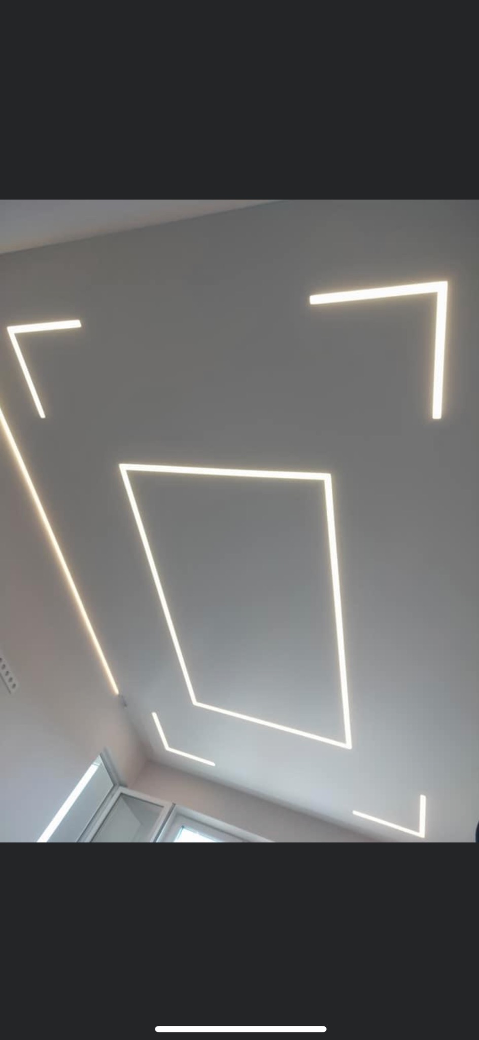 Biały sufit z wpuszczonymi liniowymi oprawami LED tworzącymi geometryczne wzory: kwadrat, kąty proste i linie. Widoczne fragmenty okna.