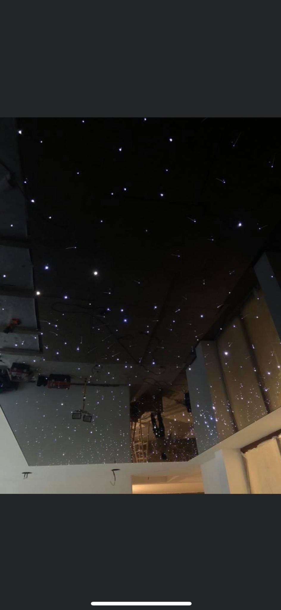 Błyszczący sufit z efektem gwiazd, widok z dołu, białe ściany, odbicie pomieszczenia w suficie, drabina w tle, prace wykończeniowe w trakcie.