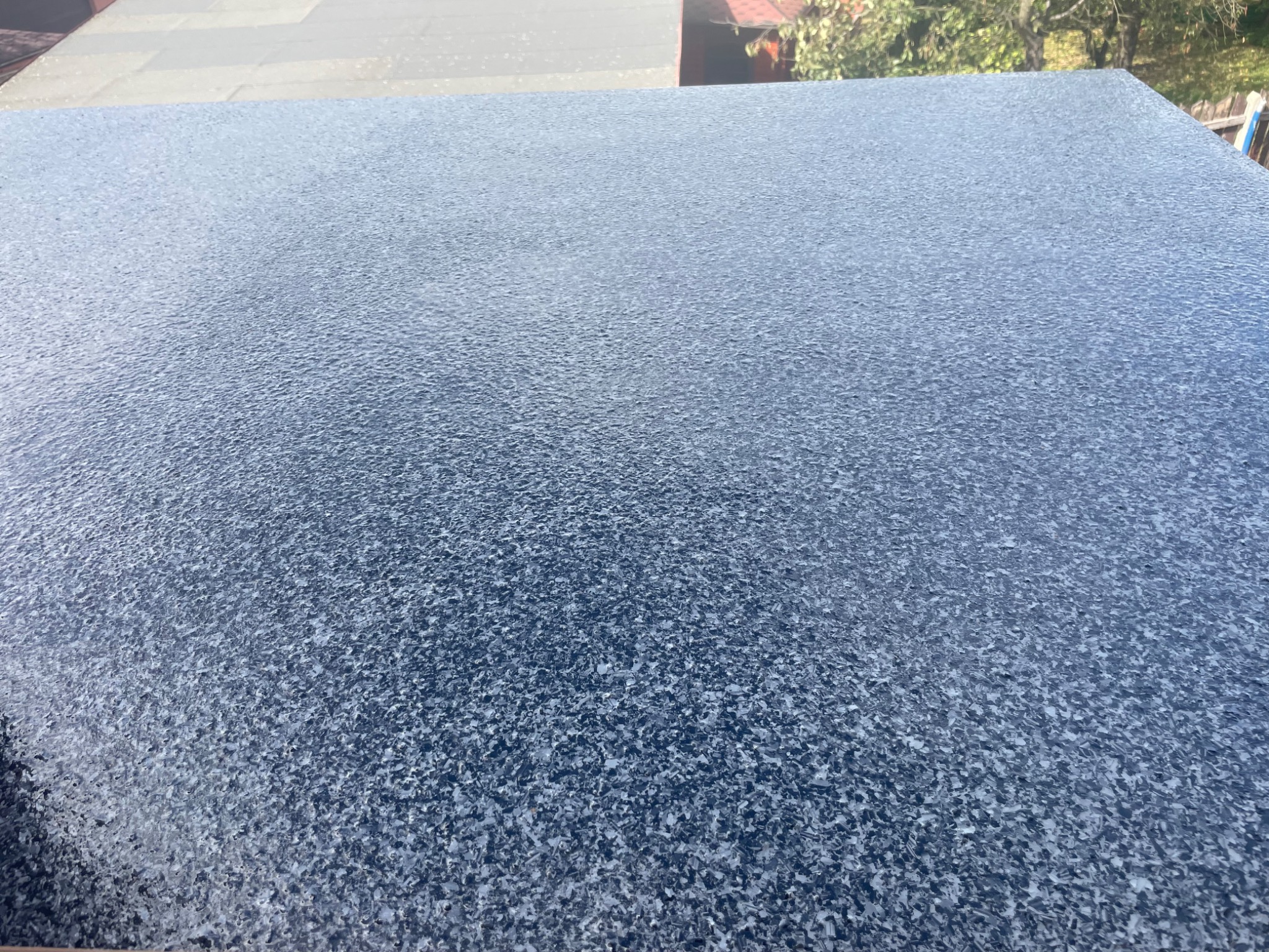 Granitowa posadzka żywiczna w odcieniach szarości, z delikatnym połyskiem, widziana z góry, z elementami budynku w tle.