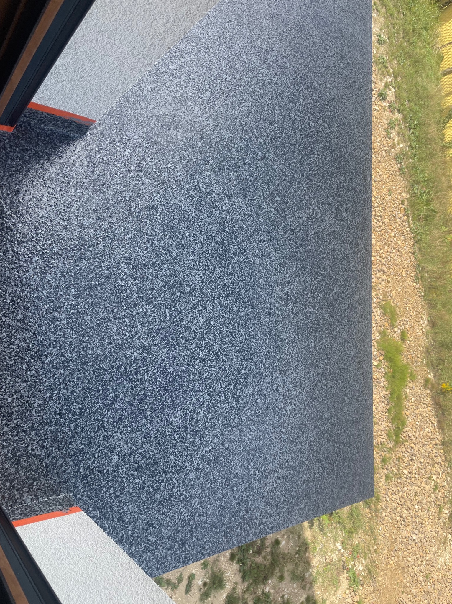 Szara, drobnoziarnista posadzka żywiczna na balkonie, widok z góry, z fragmentem balustrady i otoczenia zewnętrznego.