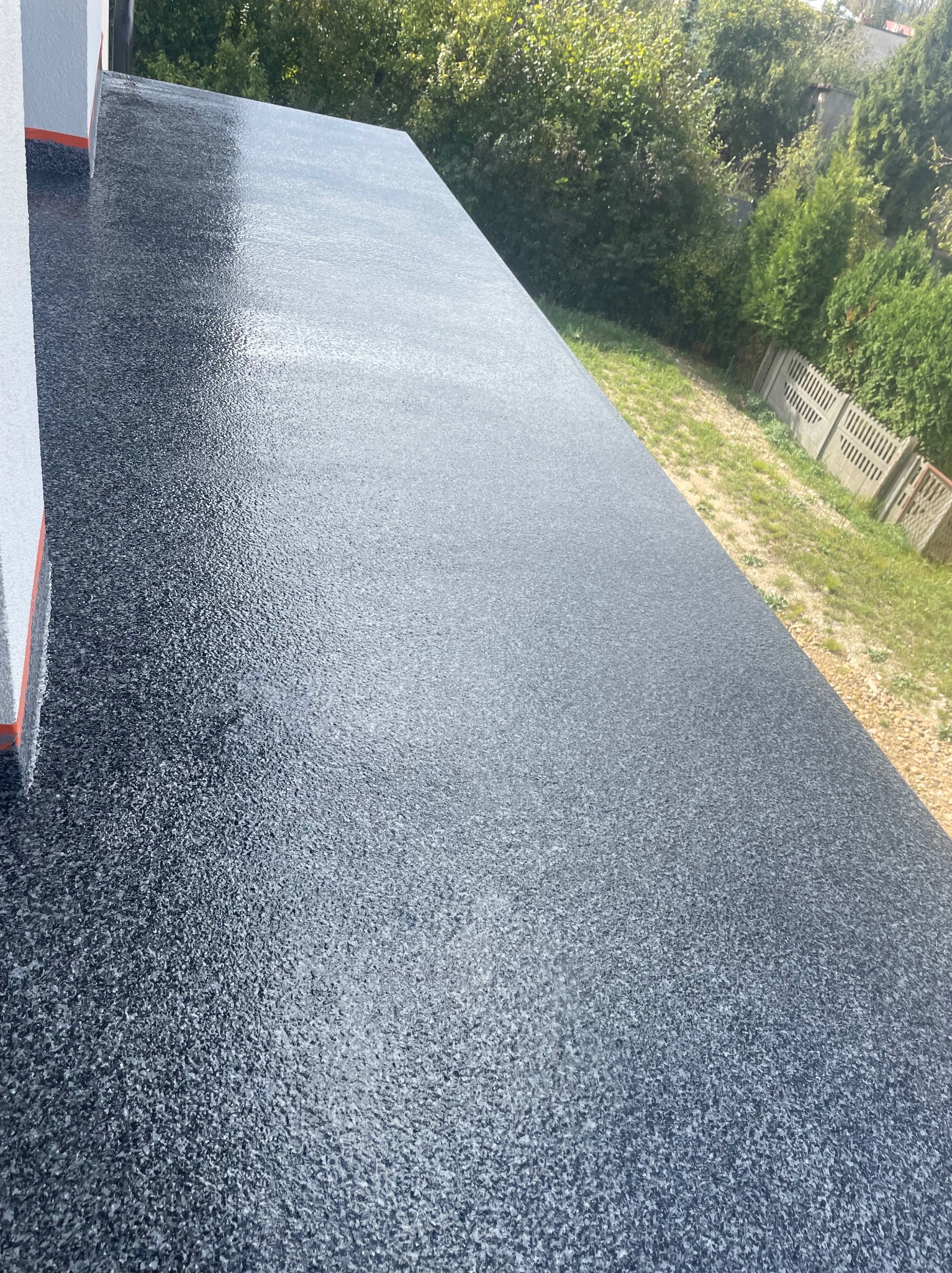 Szara, błyszcząca posadzka żywiczna na tarasie, widok z góry na zewnątrz, z fragmentem elewacji budynku i zieleni w tle.