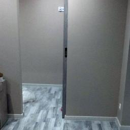 Cztery Kąty - Wnętrze pokoju po remoncie z szarą podłogą imitującą drewno, szare ściany i przesuwnymi drzwiami w ościeżnicy.